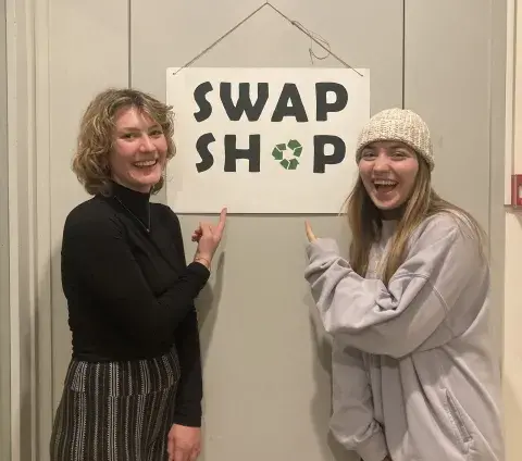 GO Scholar Skylar + volunteer Siri pose with the Swap Shop sign 